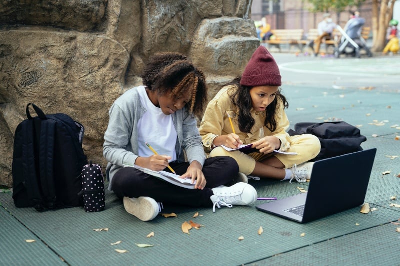 Two children study outside on connected laptops